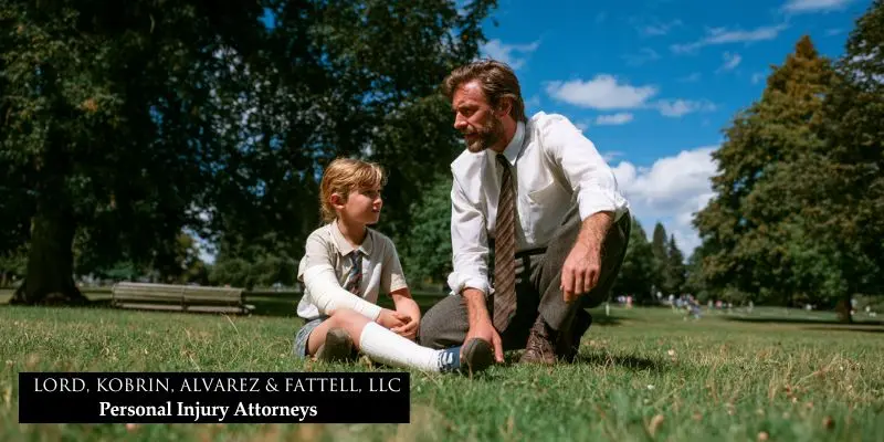 A lawyer kneels beside an injured child with a bandage, joyfully playing together in a sunny park field.